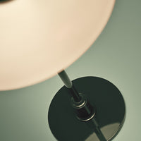 Black lamp base with a sleek, modern design and a soft, glowing white shade against a muted green background.