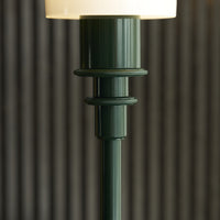 Green ribbed lamp base with a glossy finish, topped by a soft white lampshade, set against textured striped background.