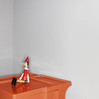 "Orange storage box with a playful, colorful Pinocchio figure against a soft gray wall."
