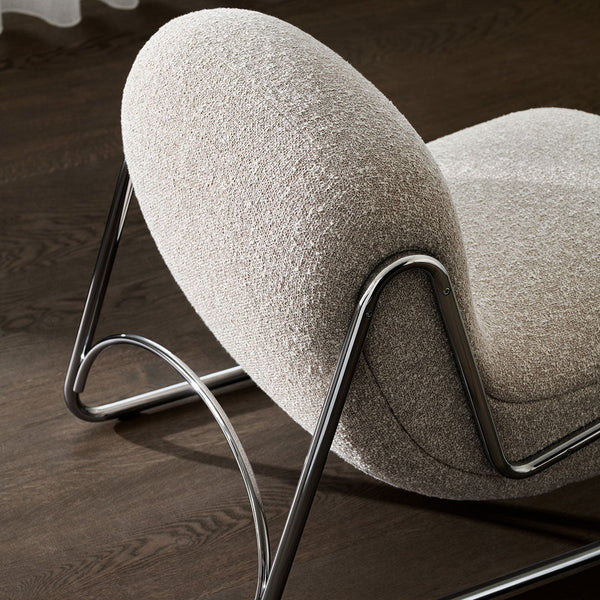 Beige textured chair with rounded shape and sleek chrome legs on a dark wood floor. Modern and minimalist design.