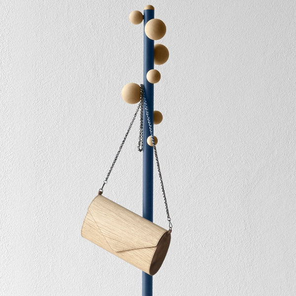 Light wood cylindrical bag hanging on a blue pole with natural wood balls, minimalistic design and soft textures.