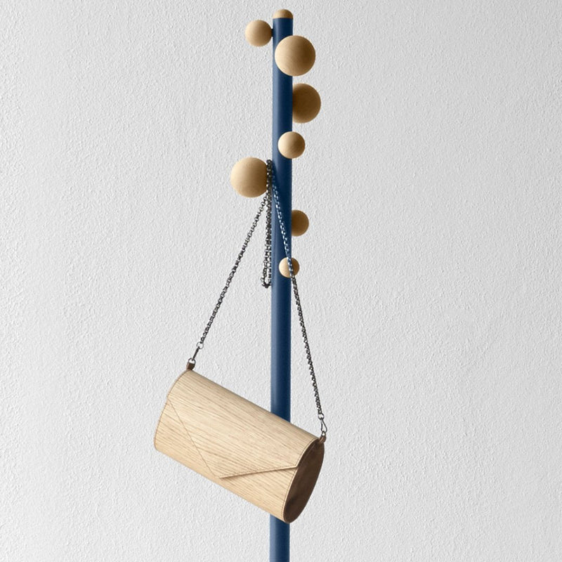 Light wood cylindrical bag hanging on a blue pole with natural wood balls, minimalistic design and soft textures.