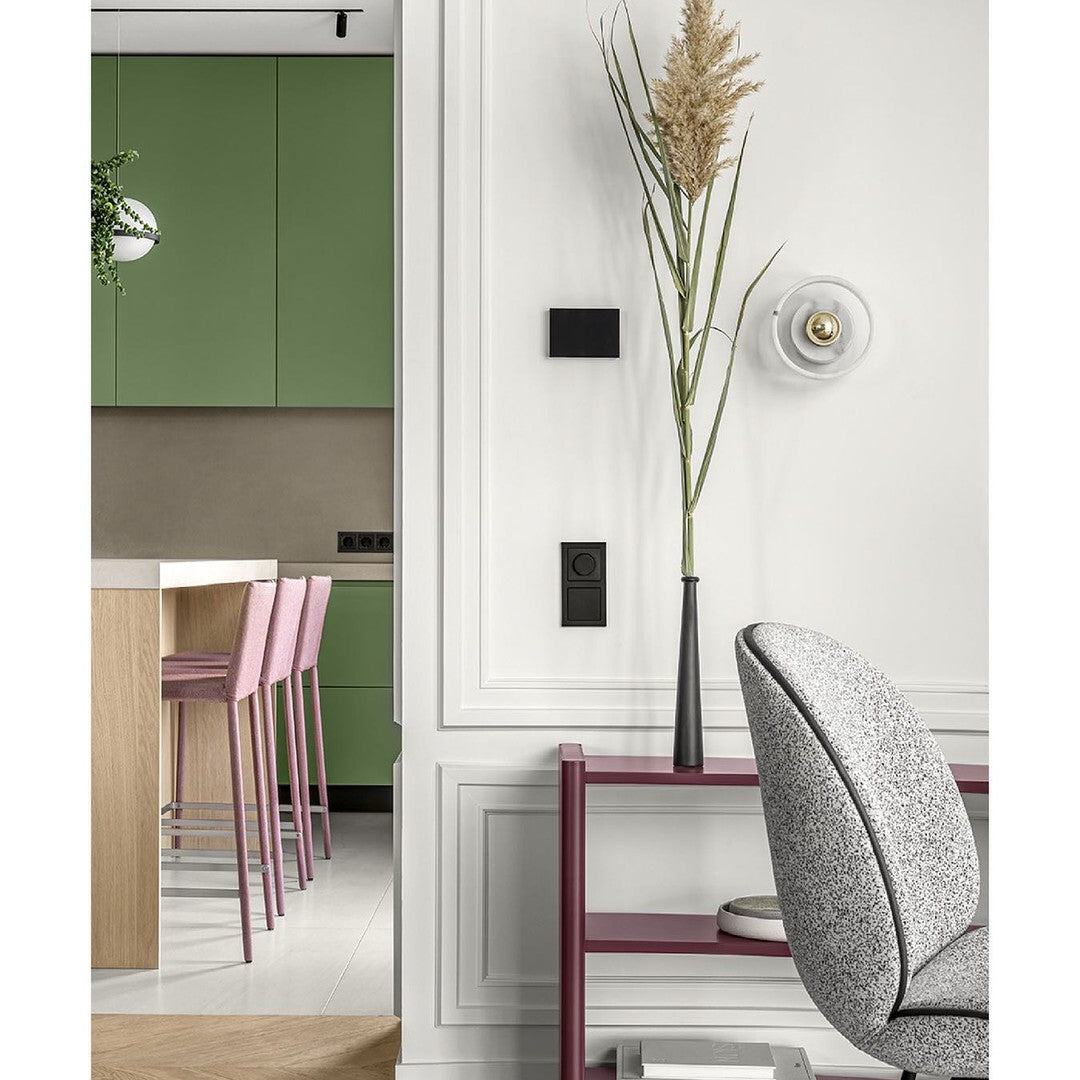 "Modern interior with green cabinets, pink bar stools, and a gray patterned chair against a white wall."