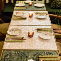 Elegant table setting with light patterns, green table linens, pastel plates, and warm candlelight ambiance.