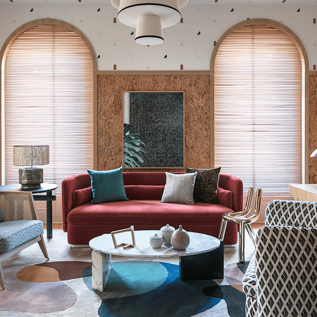 Modern living room featuring a red sofa, vibrant blue and patterned cushions, and a multicolored geometric rug.