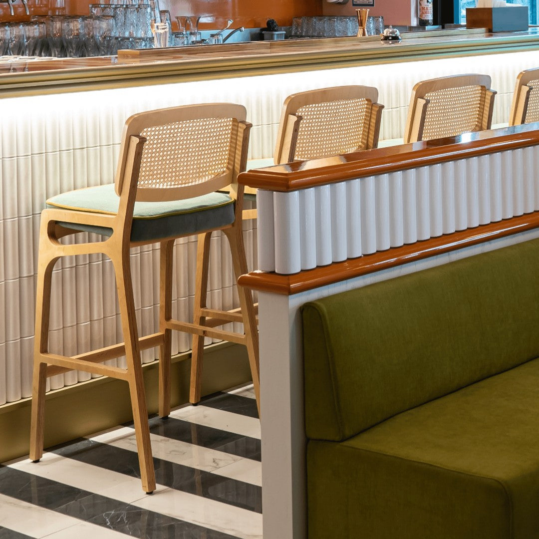Light wood bar stool with green cushion, contrasting white and oak tones, set against a black and white striped floor.