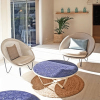 "Cozy living room with beige chairs, blue accent pillows, a round blue patterned table, and a natural fiber rug."