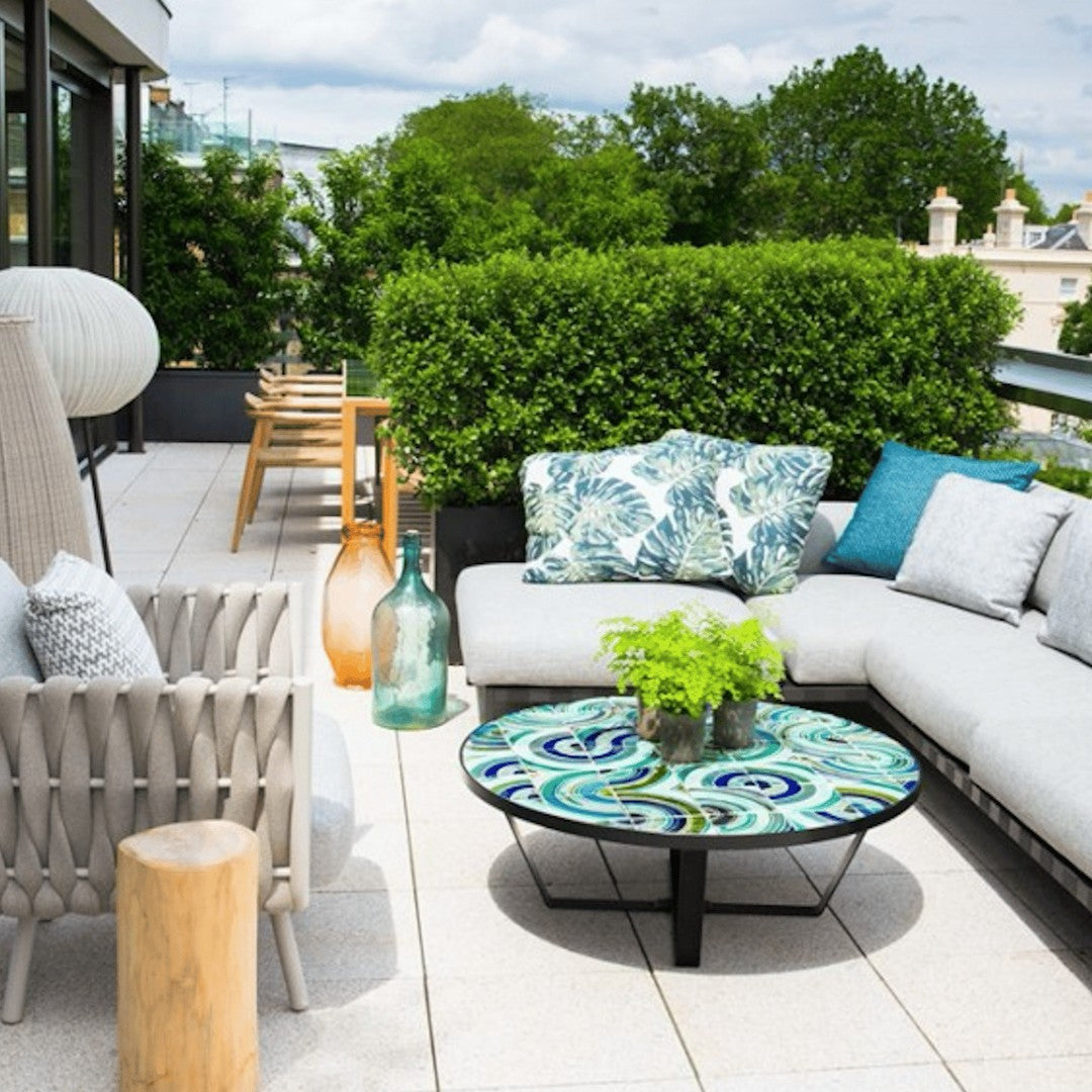 "Cozy outdoor seating with blue and green patterned cushions, vibrant table, and natural wood accents on a sunny terrace."