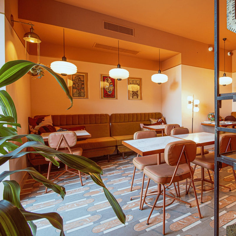 Modern cafe interior with warm orange walls, green seating, and a patterned floor featuring earthy tones and geometric designs.