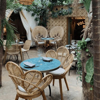 Bohemian-style dining area featuring teal table, natural wicker chairs, leafy greenery, and earthy tones.