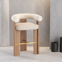 Beige upholstered bar chair with natural wood legs and gold accent, displayed in a modern minimalist setting.