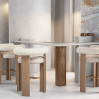Modern bar table with gray top, natural wood legs, and cream upholstered stools on a light gray concrete floor.