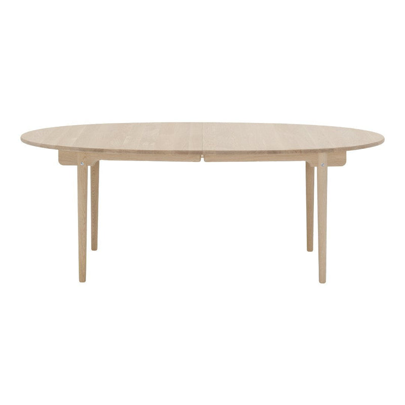 Light beige oval dining table with a smooth, minimalist surface and natural wood grain, supported by sleek legs.