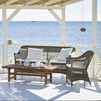 "Coastal outdoor furniture set with a natural wicker texture and soft white cushions against a serene blue ocean backdrop."