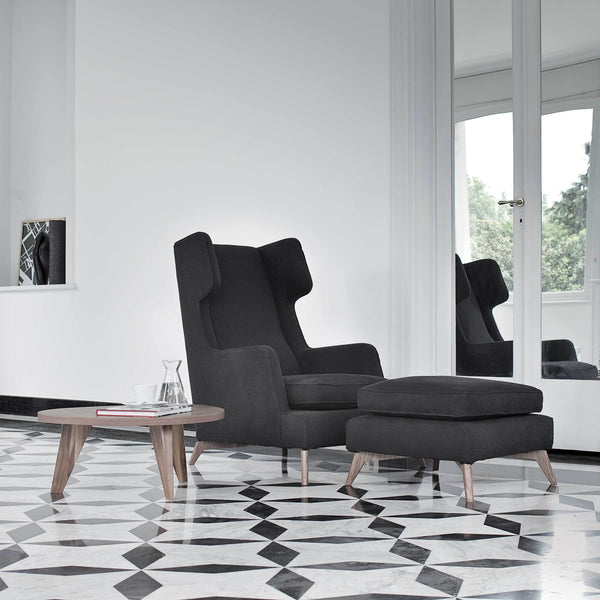 Gray upholstered chair with matching ottoman, set against a black and white geometric patterned floor.