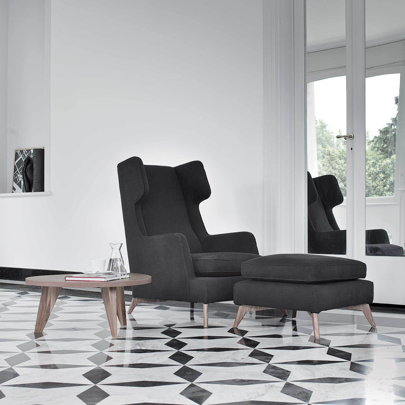 Gray upholstered chair with matching ottoman, set against a black and white geometric patterned floor.