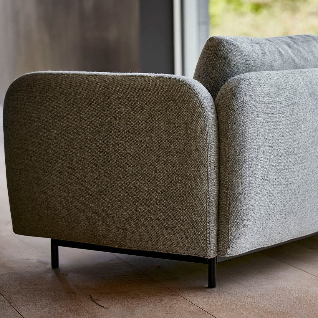 Gray upholstered sofa with rounded edges and minimalistic design, featuring a textured fabric and sleek black legs.