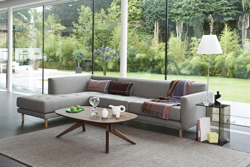 Modern gray sectional sofa with multicolored throw blankets, paired with wooden accent table and neutral area rug.