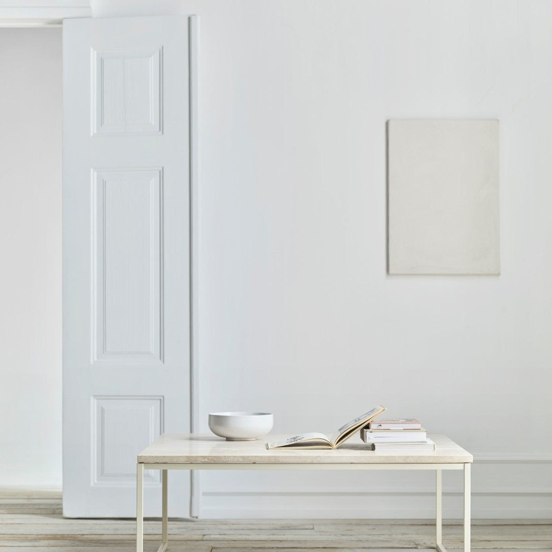 Minimalist interior with soft white walls, light wood floor, and a simple cream-colored table.