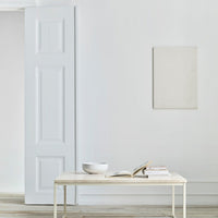 Minimalist interior with soft white walls, light wood floor, and a simple cream-colored table.