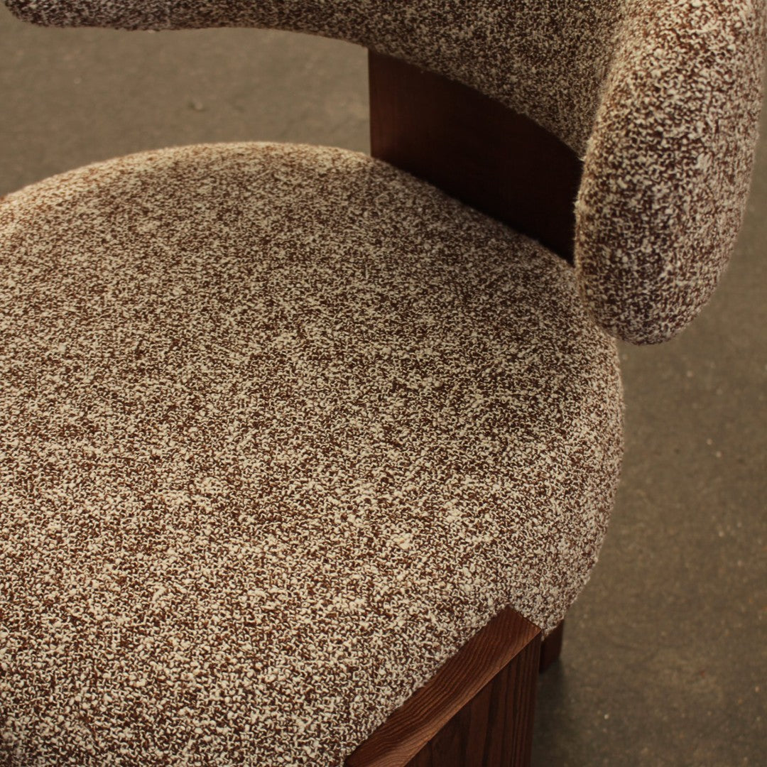 Brown textured upholstery with a speckled pattern on a cushioned chair seat and curved backrest.