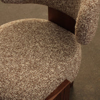 Brown textured upholstery with a speckled pattern on a cushioned chair seat and curved backrest.