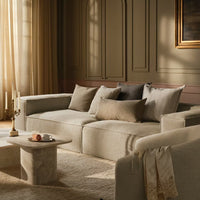 Soft beige sofa with neutral-toned cushions, featuring a modern minimalist design against warm, muted walls.
