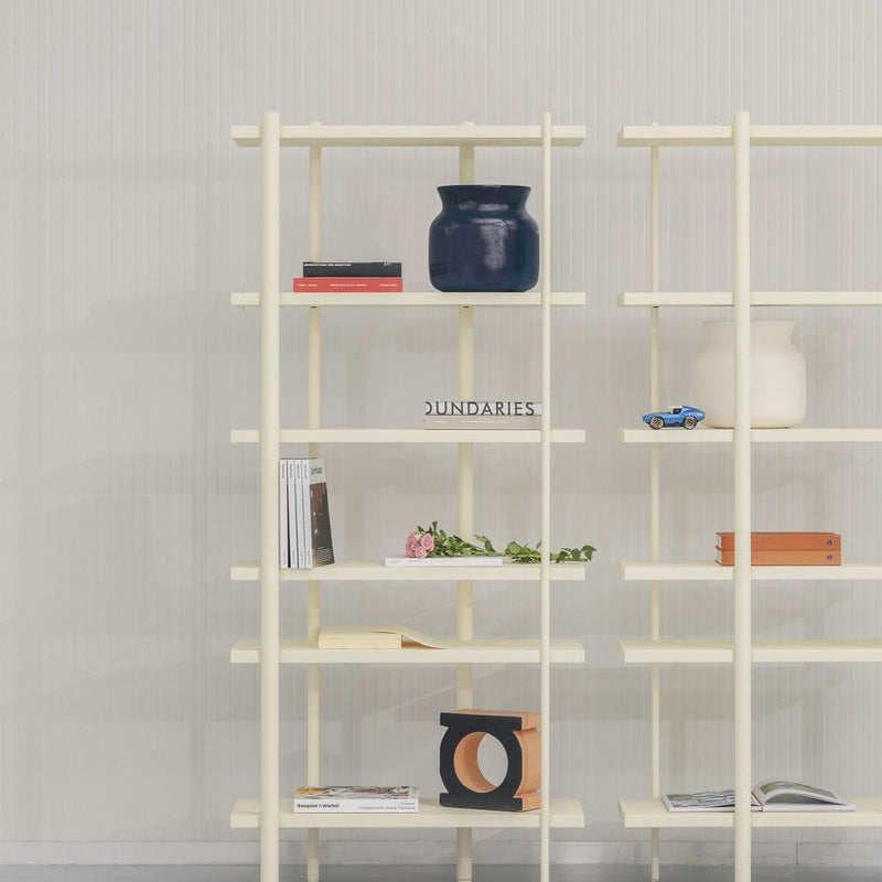 Cream-colored shelving unit with navy blue vase, orange accents, and subtle green foliage among decorative items.