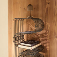 Black wire shelving unit with flowing curves, set against a warm wood backdrop. Stylish and modern design.
