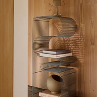 Stylish grey metal bookshelf with curved lines, set against warm wooden tones and soft shadows. Ideal modern decor.