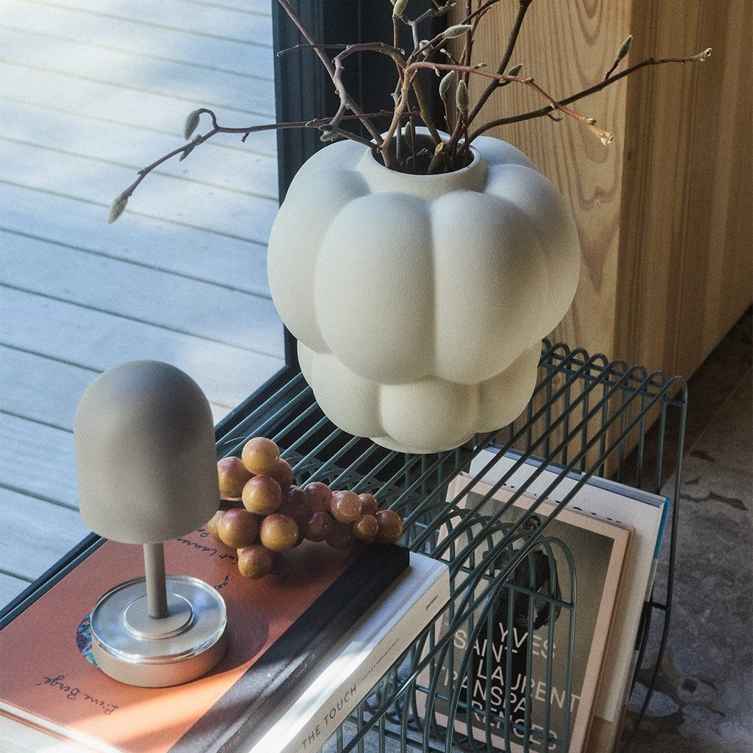 Gray matte textured vase and dome-shaped decor on a wire table, complemented by soft purple grapes and books.