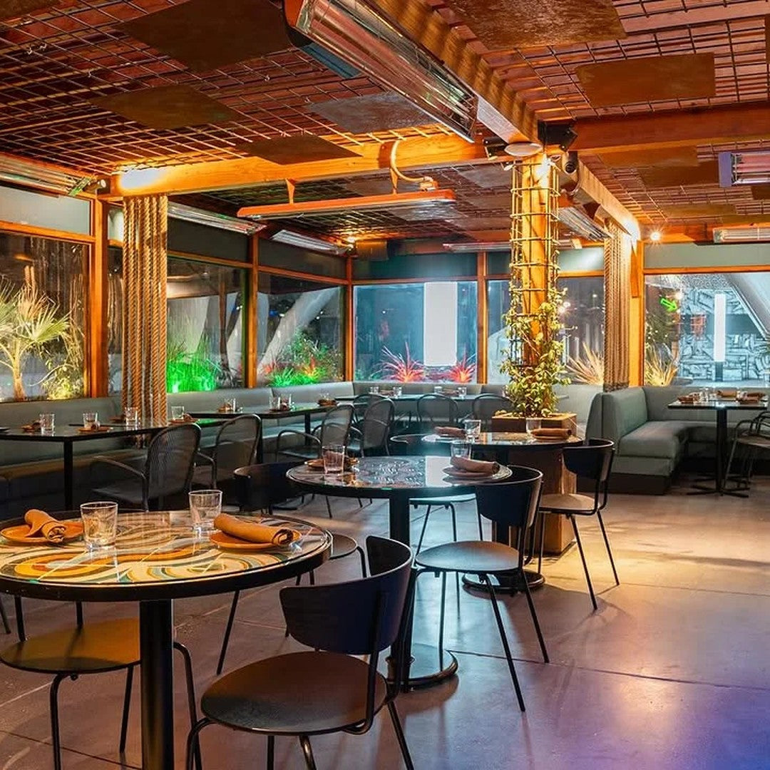 "Chic restaurant interior featuring warm wooden tones, stylish black chairs, and vibrant green plants against muted gray walls."