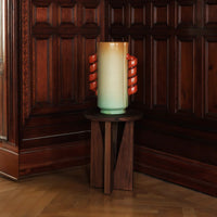 Ceramic vase in blue gradient with orange swirl handles, displayed on a wooden stand against a rich wooden backdrop.