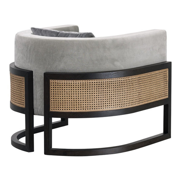 Curved grey velvet chair with black frame and natural rattan pattern on the backrest. Stylish and modern accent piece.