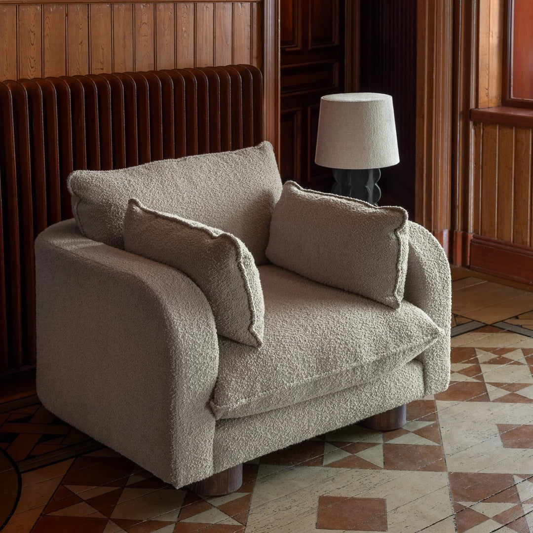 Beige textured upholstered armchair with soft cushions, showcased in a patterned floor setting.