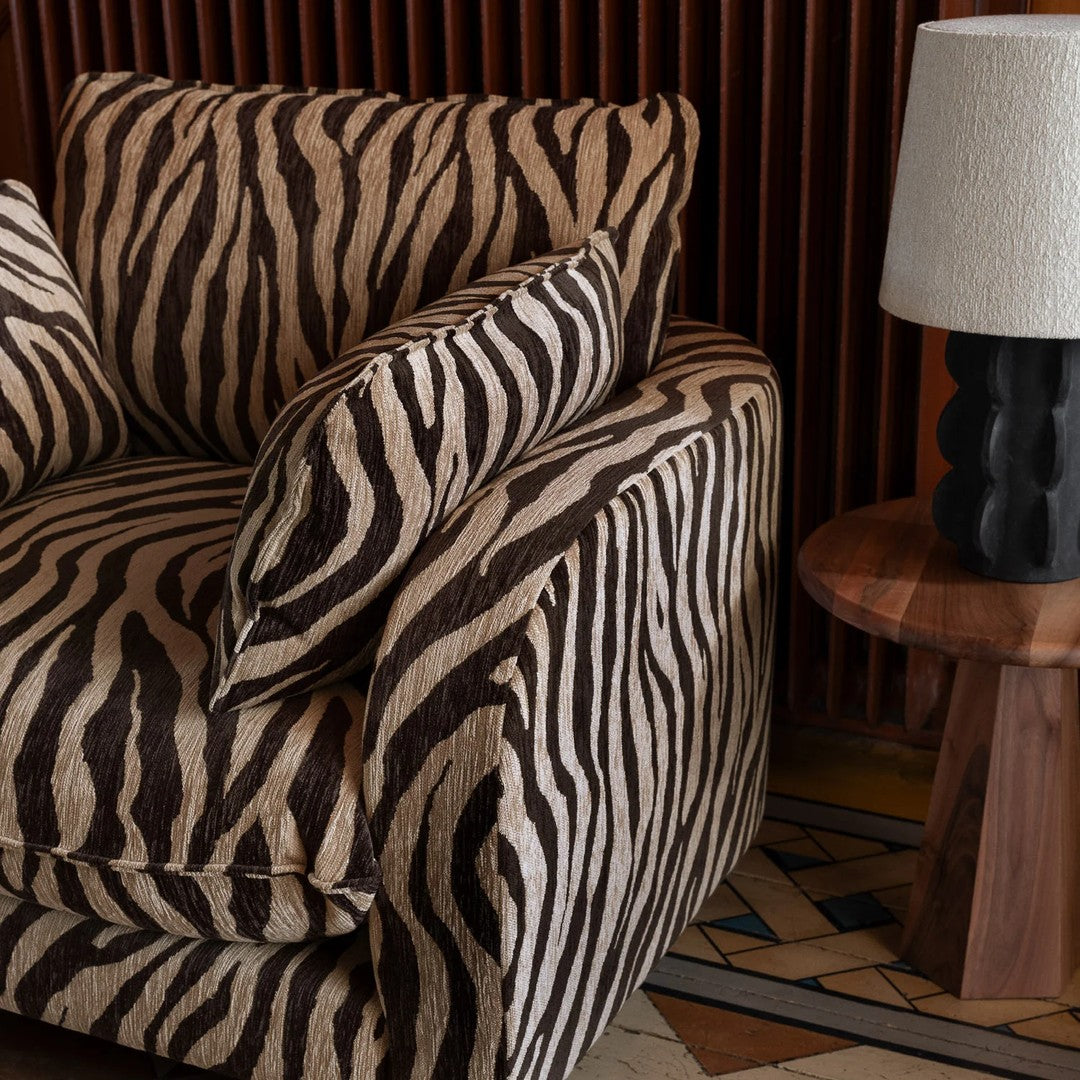 Zebra-striped couch in brown and cream tones, with contrasting solid color accents. Stylish textured fabric design.