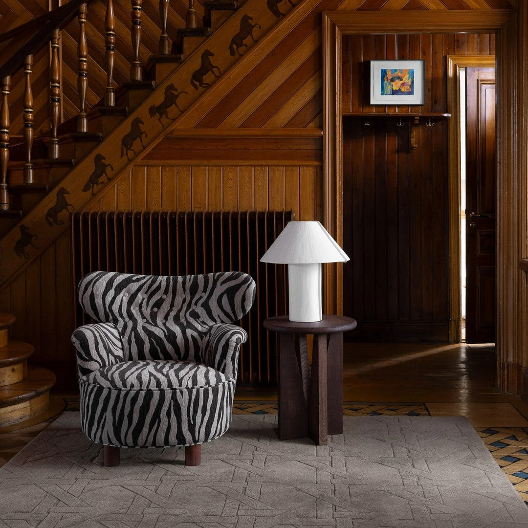 Zebra-striped armchair in black and white with a minimalist lamp and patterned rug, set against a rustic wooden interior.