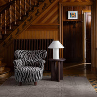 Zebra-striped armchair in black and white with a minimalist lamp and patterned rug, set against a rustic wooden interior.