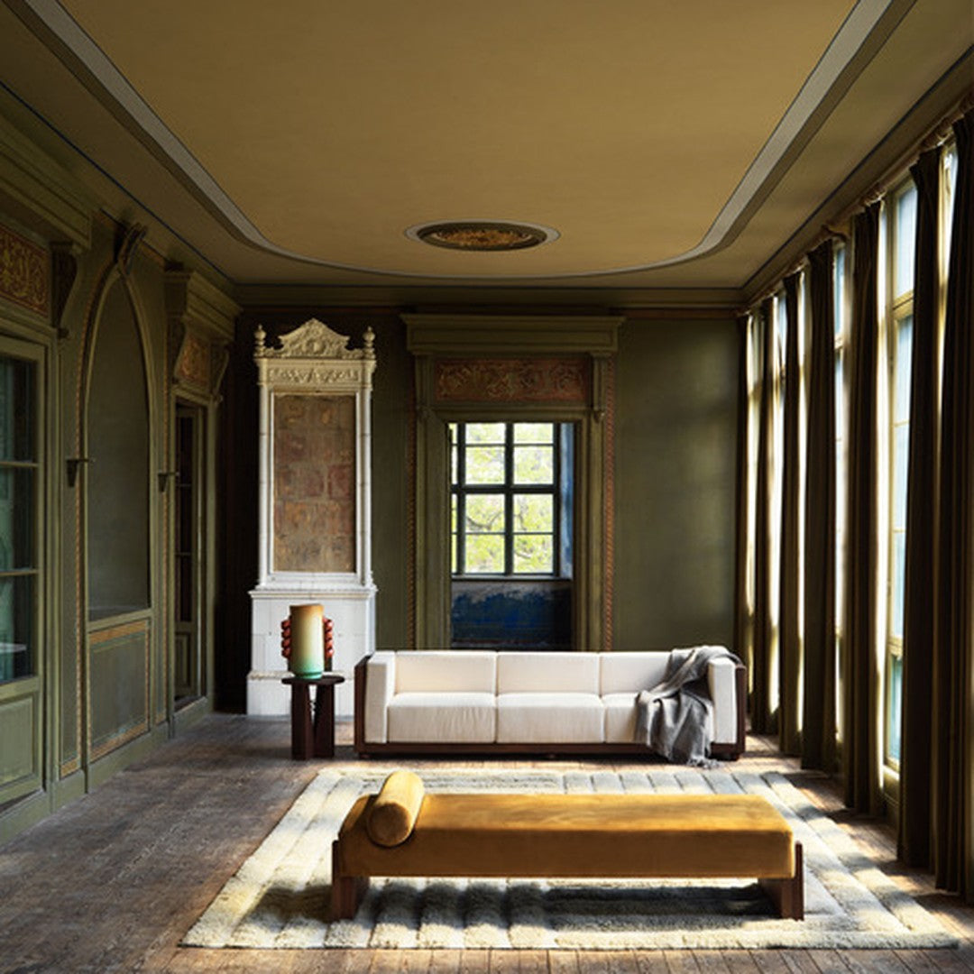 Elegant green walls with gold accents, complemented by a beige sofa and mustard yellow bench, featuring natural light.