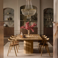Wooden dining table with a light oak finish, paired with dark chairs and a crystal chandelier, adorned with pink floral decor.