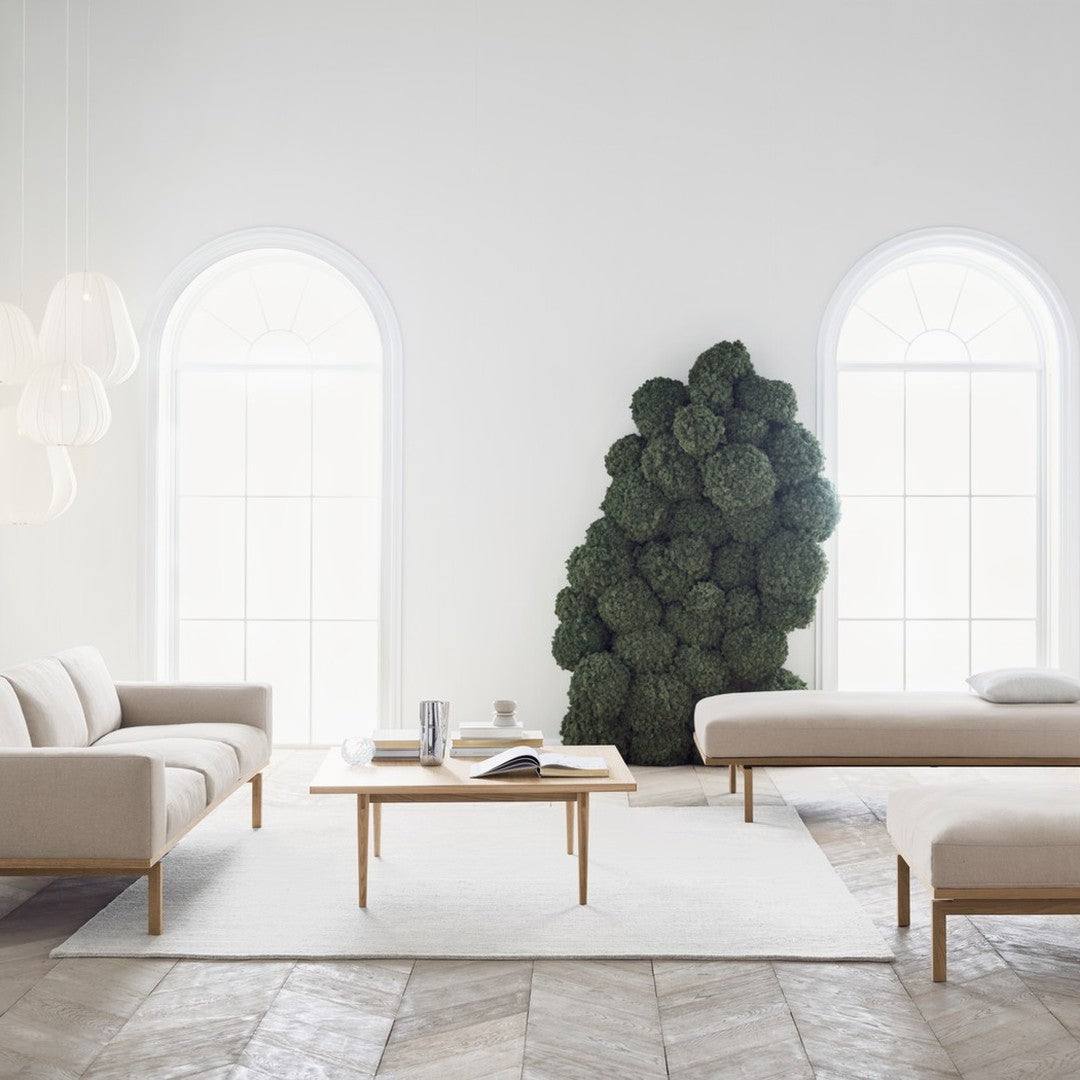 Beige sofas with light wood accents, white rug, and greenery create a modern, serene living space.