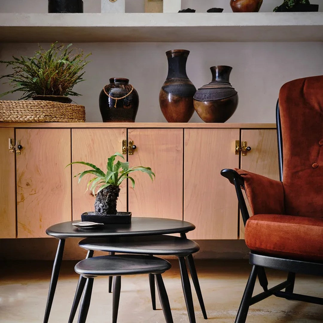 "Warm terracotta chair, natural wood cabinet, sleek black nesting tables, and earthy vases enhance a cozy interior."