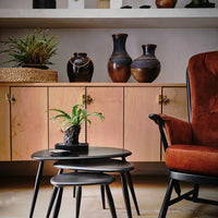 "Warm terracotta chair, natural wood cabinet, sleek black nesting tables, and earthy vases enhance a cozy interior."