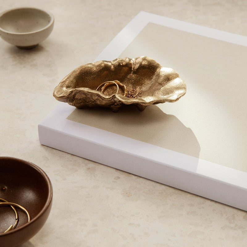 Gold organic-shaped dish on a white surface, surrounded by earthy brown and muted gray ceramic items.
