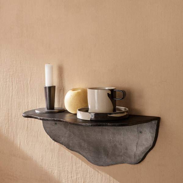 Black shelf with natural texture, featuring a white candle, yellow apple, and a striped black-and-white cup and saucer.
