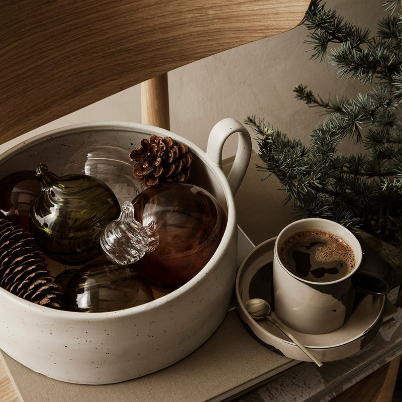 "Muted earth tones in a bowl with glass ornaments, pinecones, and a cup featuring a soft, neutral color palette."