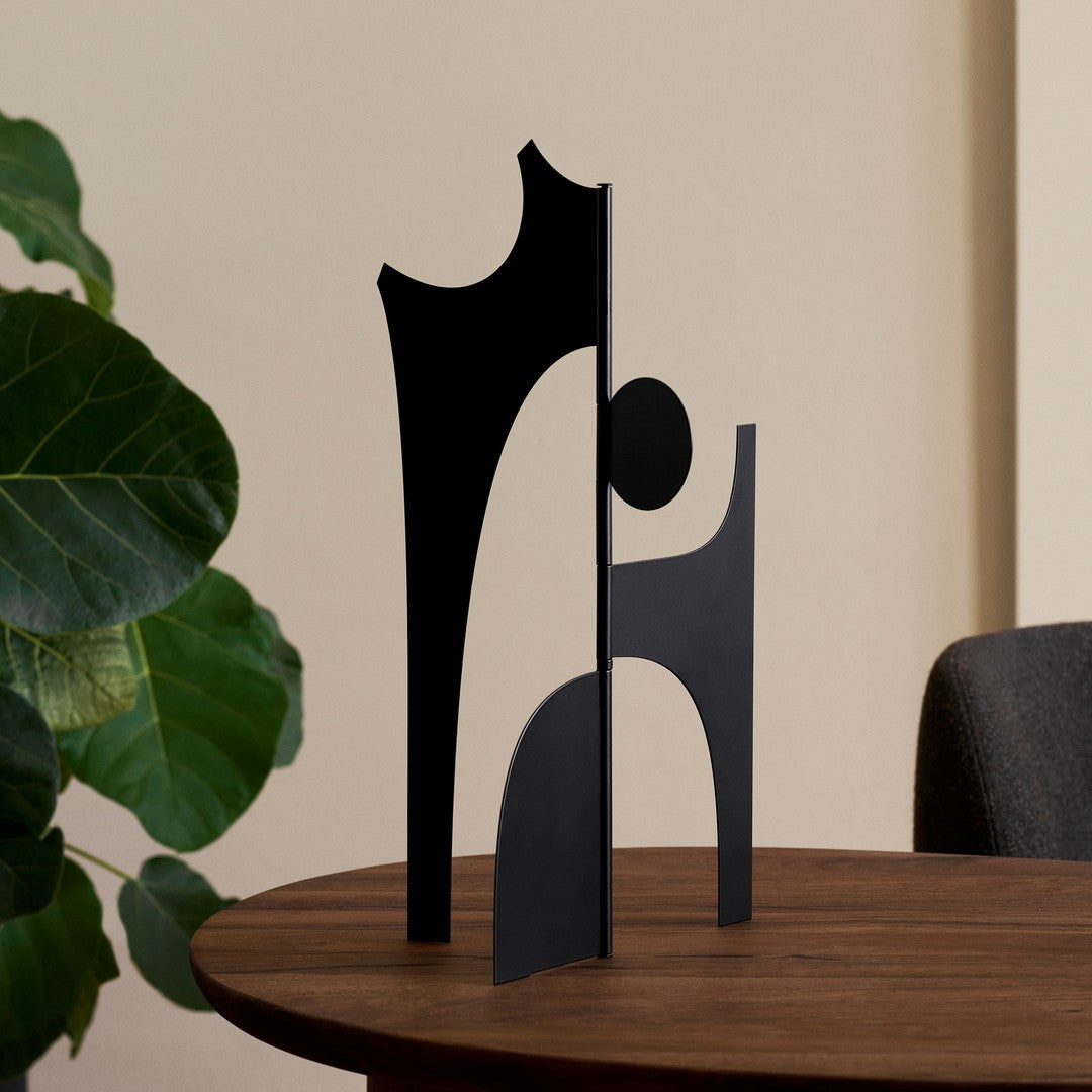 Abstract black metal sculpture with geometric shapes on a wooden table, creating a modern artistic vibe.