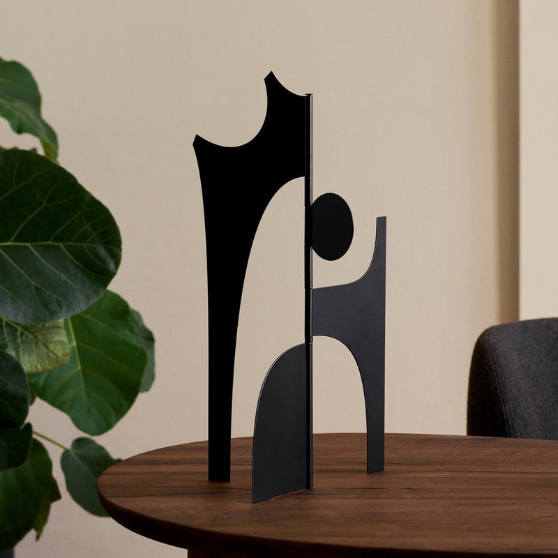 Abstract black metal sculpture with geometric shapes on a wooden table, creating a modern artistic vibe.