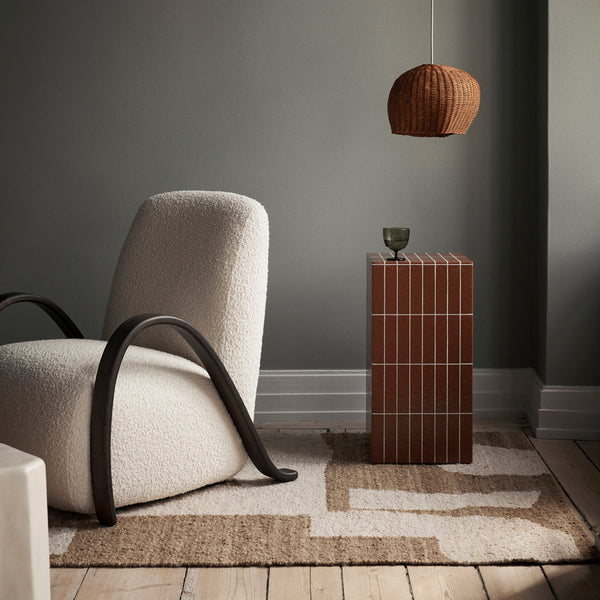 Cozy cream and brown chair with a textured, abstract rug and a striped amber-colored side table in a muted setting.