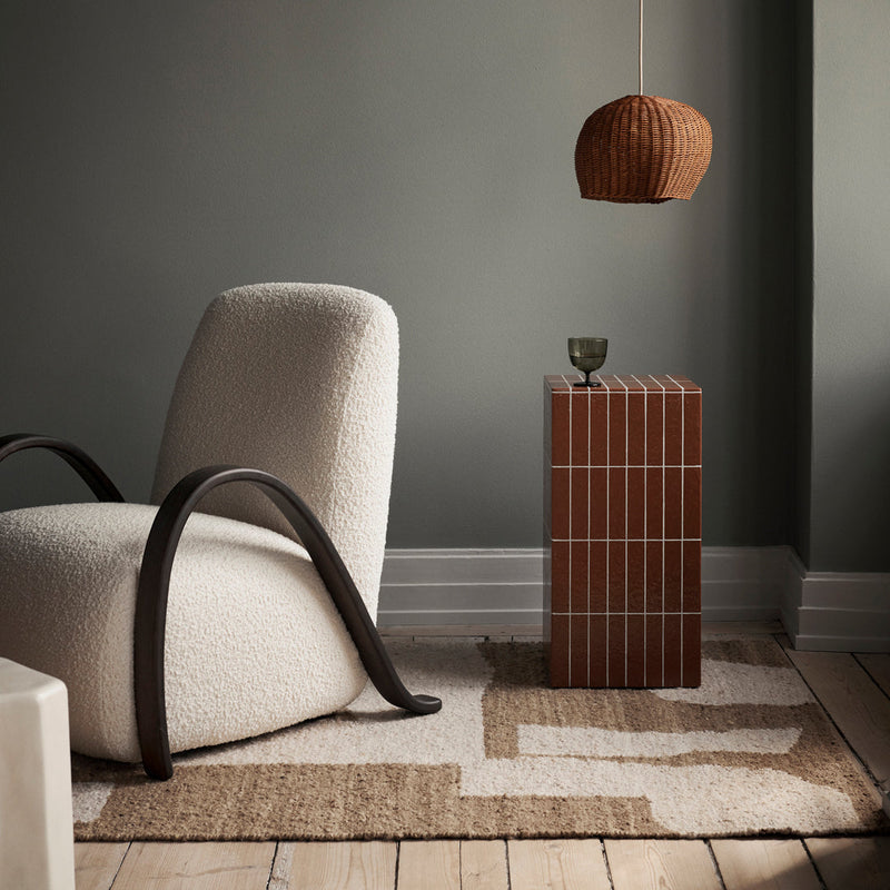 Cozy cream and brown chair with a textured, abstract rug and a striped amber-colored side table in a muted setting.